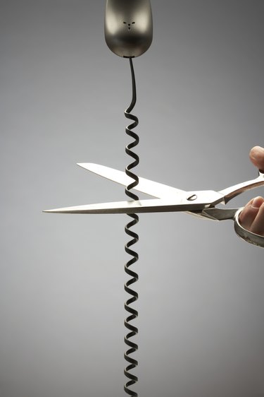 Person cutting telephone cord with scissors, close-up of hand