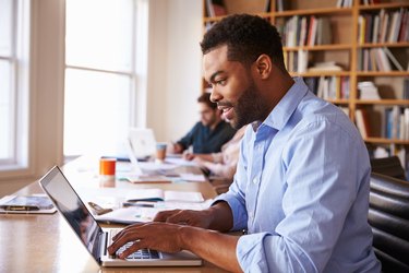 Businessman Using Laptop At Desk In Busy Office