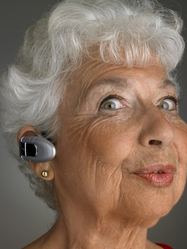 Senior woman wearing bluetooth, pulling facial expression, portrait, close-up