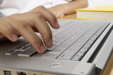 Hand on computer keyboard with yellow book, close-up