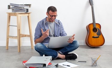 thrilled creative entrepreneur sitting on floor to work on laptop