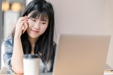 Happy asian student using smart phone and laptop at cafe