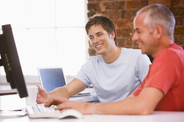 Two businessmen in office typing on computer and s