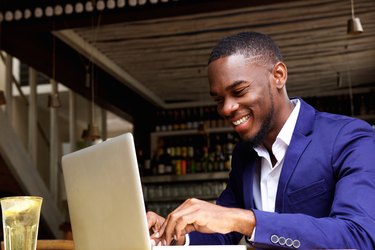 Smiling african businessman working on laptop at cafe