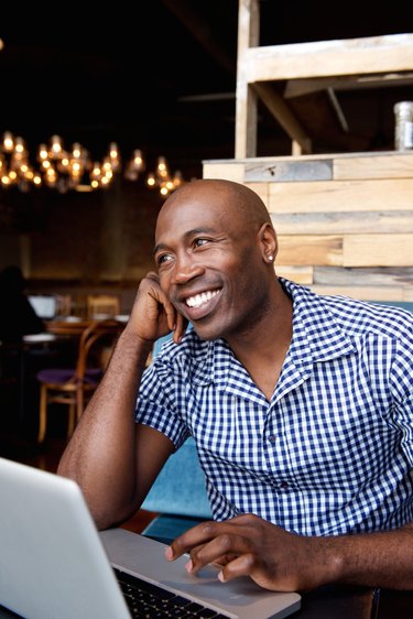 Happy african man sitting at a cafe with laptop