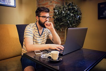 Cheerful Young Man Using Laptop In Coffee Shop