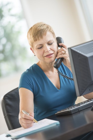Businesswoman Using Landline Phone While Working At Desk