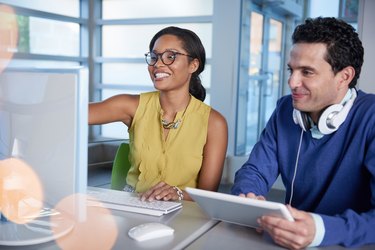 Two  colleages discussing ideas using a tablet and computer