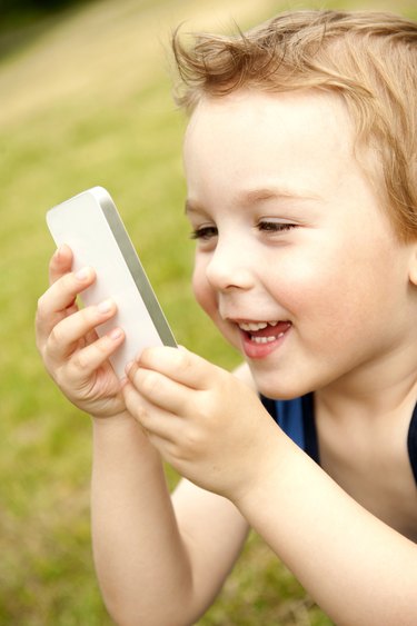 Boy holding white cell phone in park, smiling