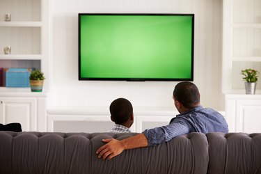 Father and son watching TV at home together, back view