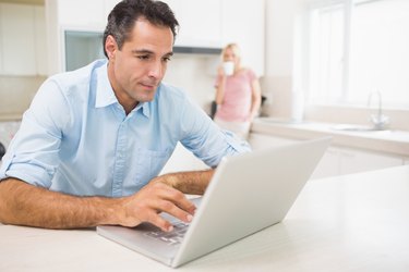 Man using laptop with woman drinking coffee at kitchen