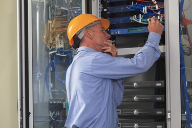 Electrical engineer working with switches and servers in broadband communication hub of electric power plant