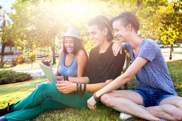 Happy friends surfing the net on laptop at the park.