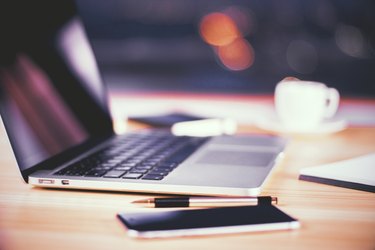 Opened laptop with smartphone, pen and cup of coffee