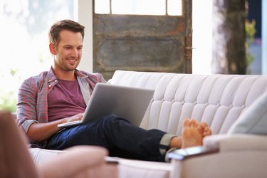 Man Relaxing On Sofa At Home Using Laptop Computer