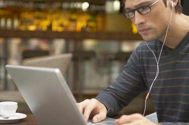 Man sitting at cafe table using laptop and wearing earphones