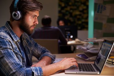 Office Workers At Desks Working Late On Laptops