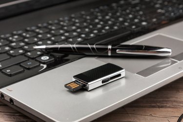 USB Flash drive lying on computer laptop keyboard and pen