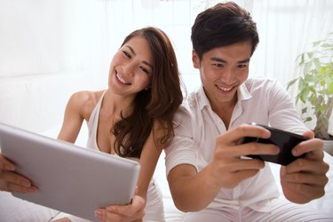 Young couple holding mobile phone and tablet computor on bed