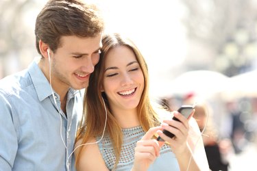 Couple sharing music from a smart phone on the street