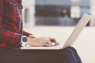 Girl wearing smartwatch using laptop outdoors