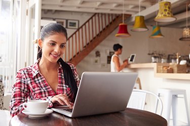 Young smiling woman with ponytail using laptop in cafe