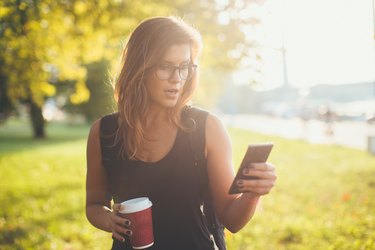 Beautiful young woman holding phone and coffee to go