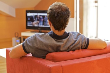 Rear view of a young man watching tv on a red chair