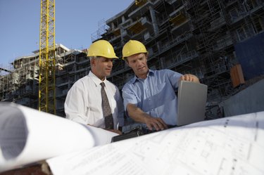 Two Men Wearing Hard Hats Looking Down at a Laptop Computer on a Building Site