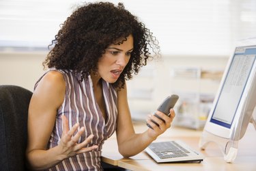 Angry businesswoman holding phone at desk