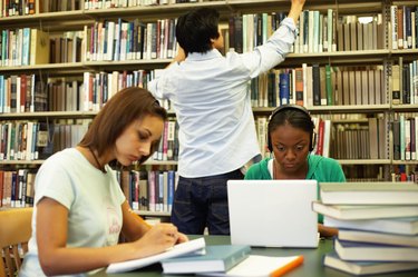 Two female students studying in library, male student in background