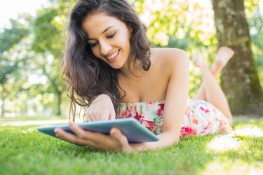 Stylish cheerful brunette lying on a lawn using tablet