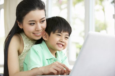 Chinese Mother And Son Sitting At Desk Using Laptop At Home