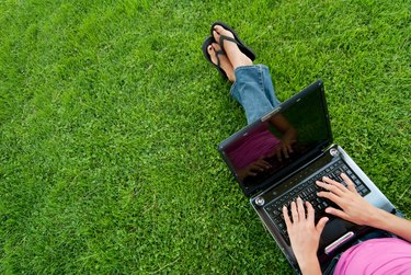 Young woman in pink on her laptop on the grass