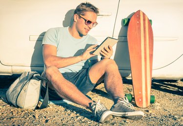 Young hipster man with tablet sitting next his car