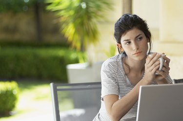 Young woman with mug thinking by laptop