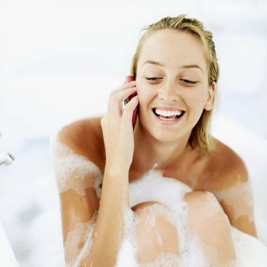 Close-up of a young woman smiling and talking on mobile phone in a bathtub