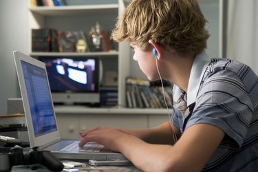 Young boy in bedroom using laptop and listening to