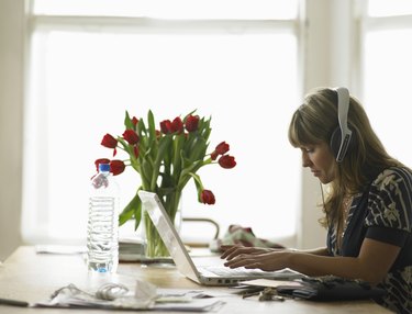 Young woman wearing headphones using laptop on dining table