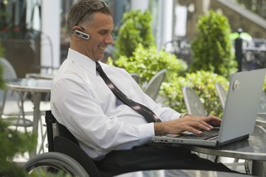 Businessman sitting in a wheelchair and using a laptop