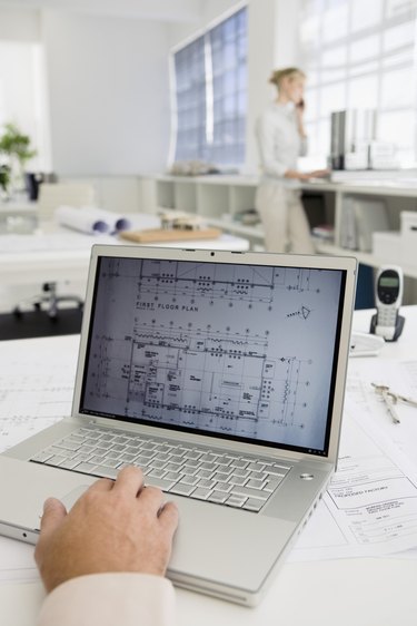 Blueprints on computer screen with businesswoman talking on cell phone