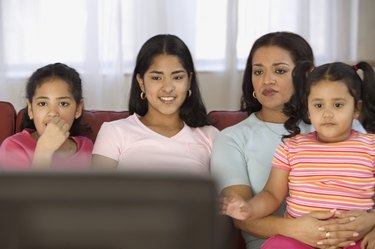 Mid adult woman watching television with her three daughters