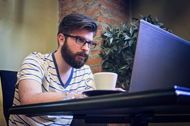 Cheerful Young Man Using Laptop In Coffee Shop