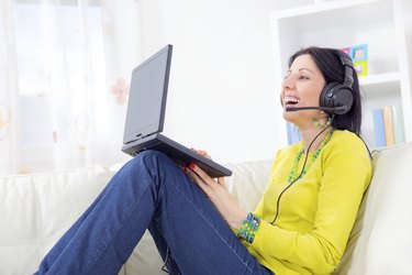 woman on sofa using laptop and headset at home