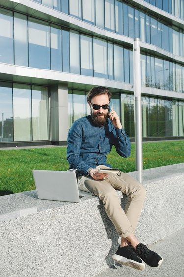 Young businessman in sunglasses with coffe laptop talking phone