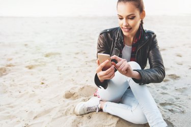 Cute, young woman using a cell phone on the sand