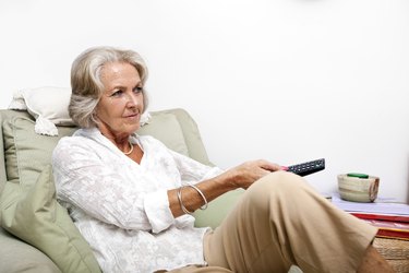 Senior woman using remote control while relaxing on armchair at home