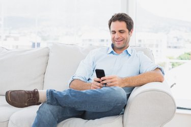 Cheerful man sitting on the couch using his smartphone