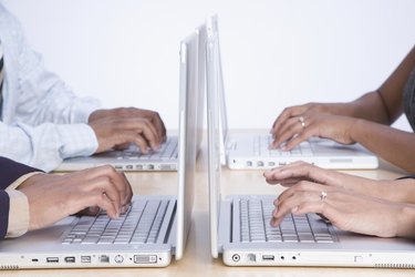 Four business people working on laptop computers, close-up on hands