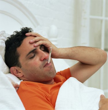 Man in bed with thermometer in mouth, holding head, eyes closed